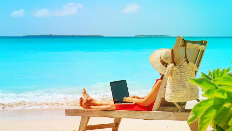 a woman sitting on a beach with a laptop