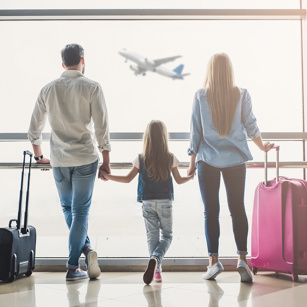 a family of three looking out an airport window at a flying plane