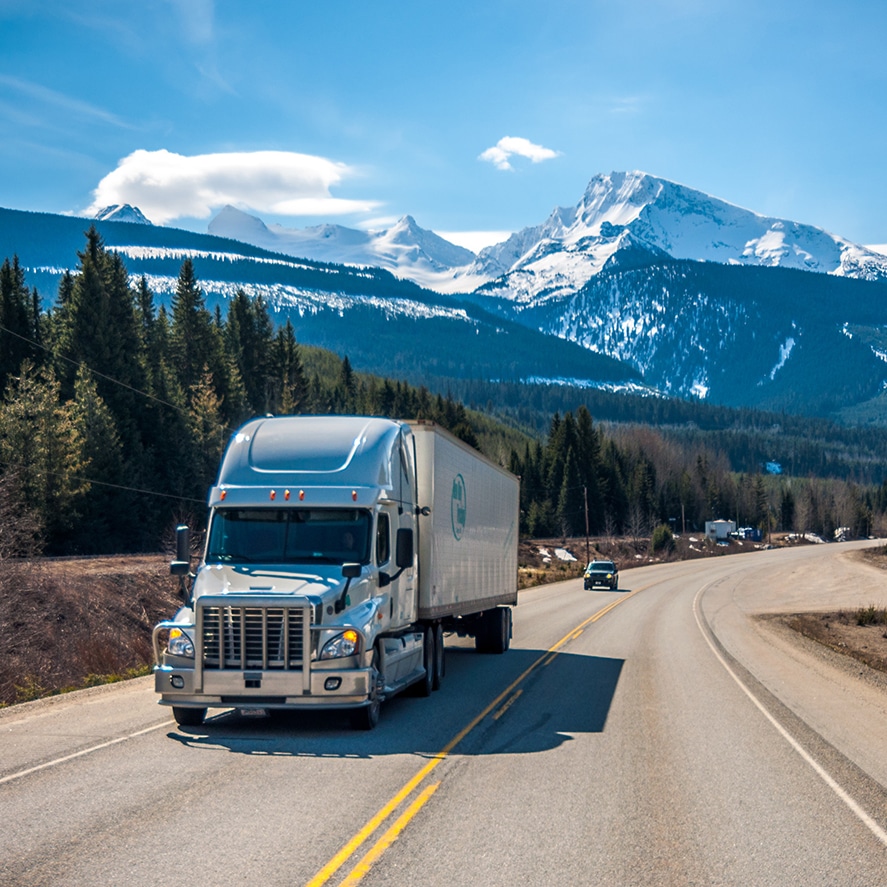 a truck driving down a road with mountains in the background