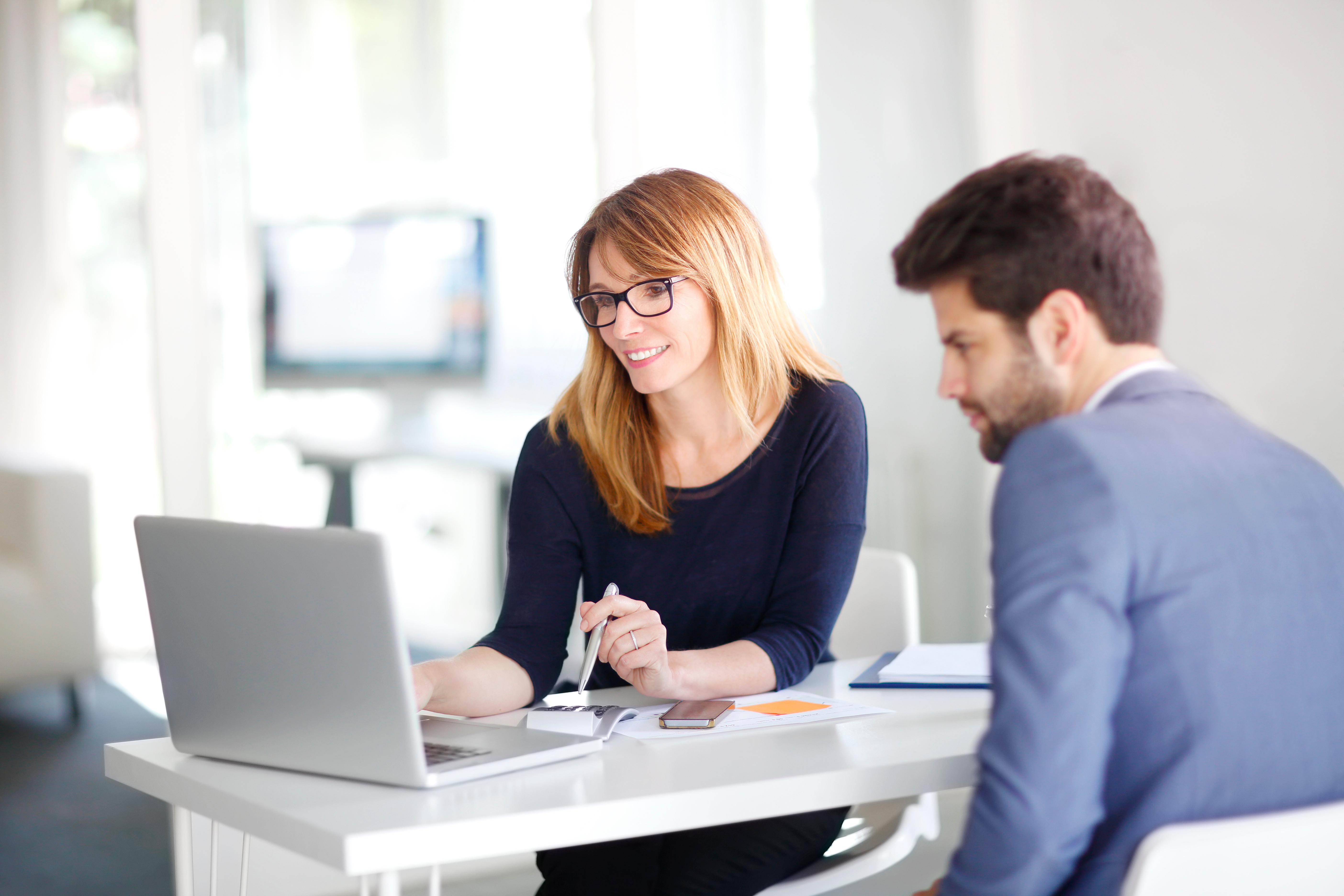 A man and a woman sitting at a desk looking at a laptop.