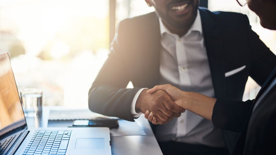 two people in suits shaking hands at a desk